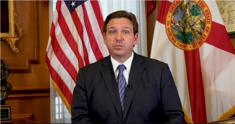 Ron DeSantis wearing a striped suit standing in front of a flag